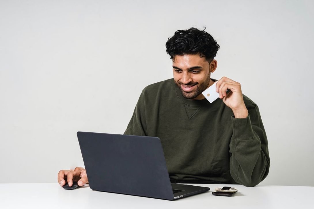 Man holding a white credit card while browsing through his laptop