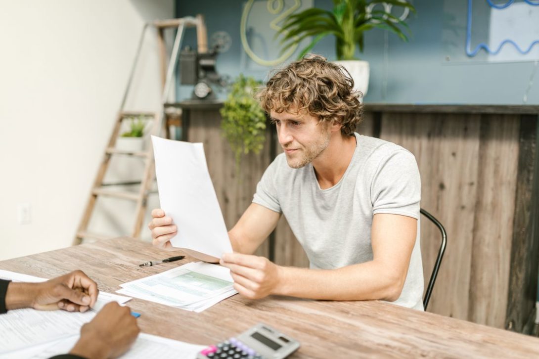 Man looking at a printed document while his friend looks on