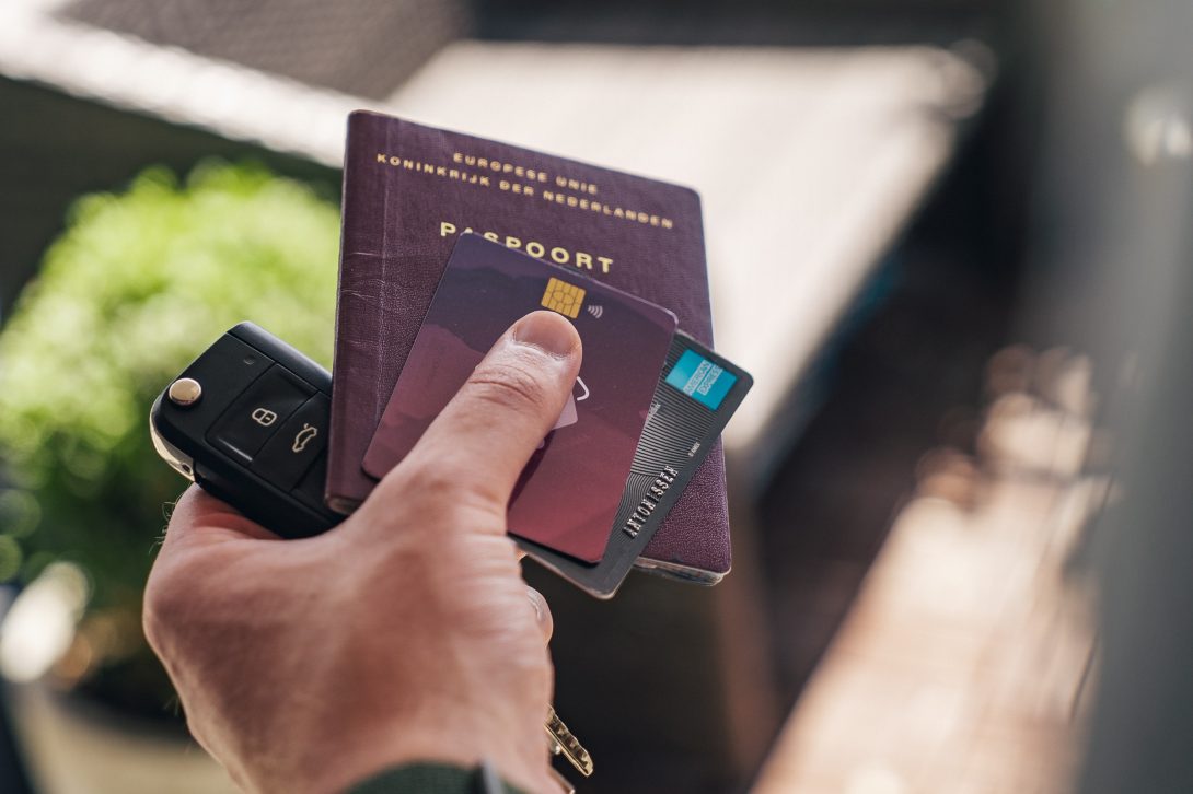 A hand of a man holding a car key, passport, and credit cards