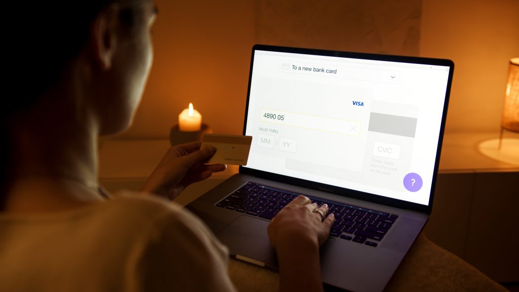 A woman holding her credit card inputting its details on a site on her laptop