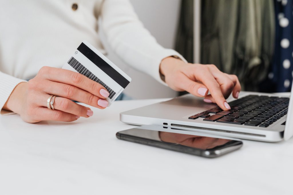 A woman holding her credit card on her right hand and typing on the laptop using her left hand