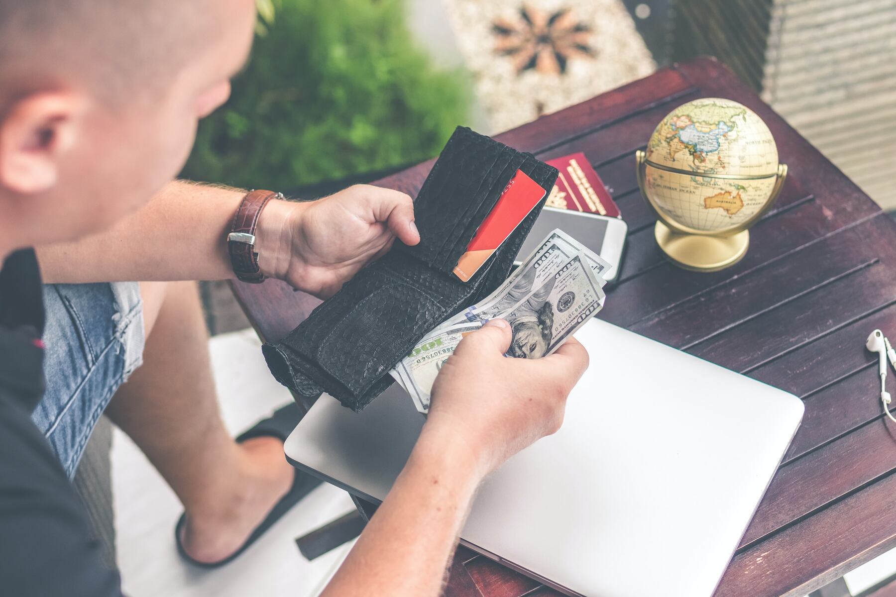 A man holding a wallet with credit cards and cash over a laptop