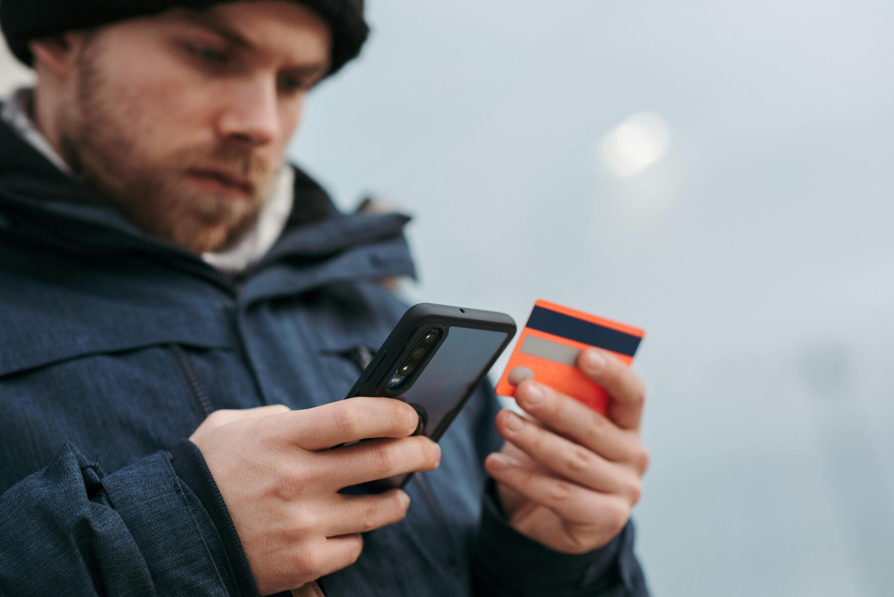 A man holding an orange credit card while using his phone