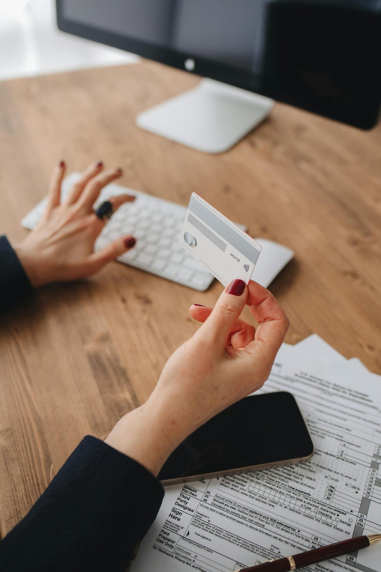 A woman sitting at a desk holding a credit card and typing on a keyboard