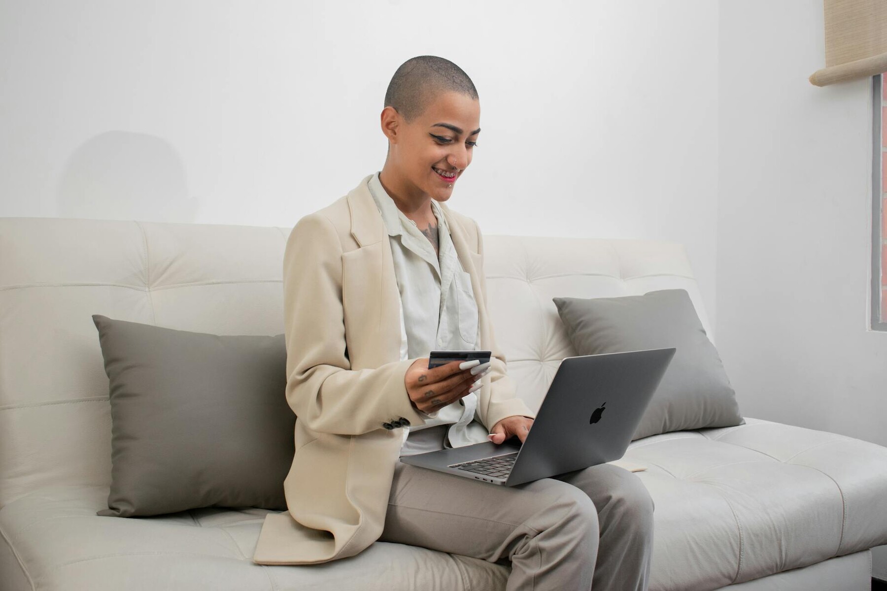 A lady in a suit holding a credit card, working on a laptop while seated on a couch
