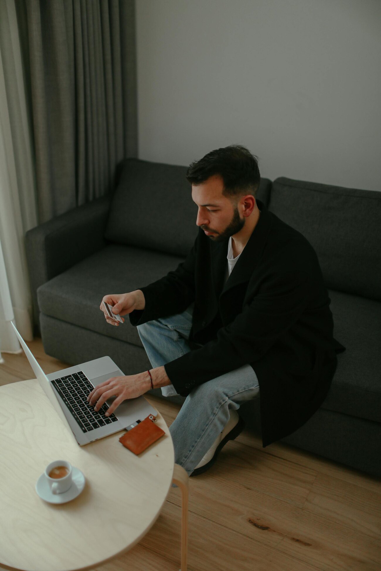 A man sitting on a couch holding a credit card, focused on using a laptop