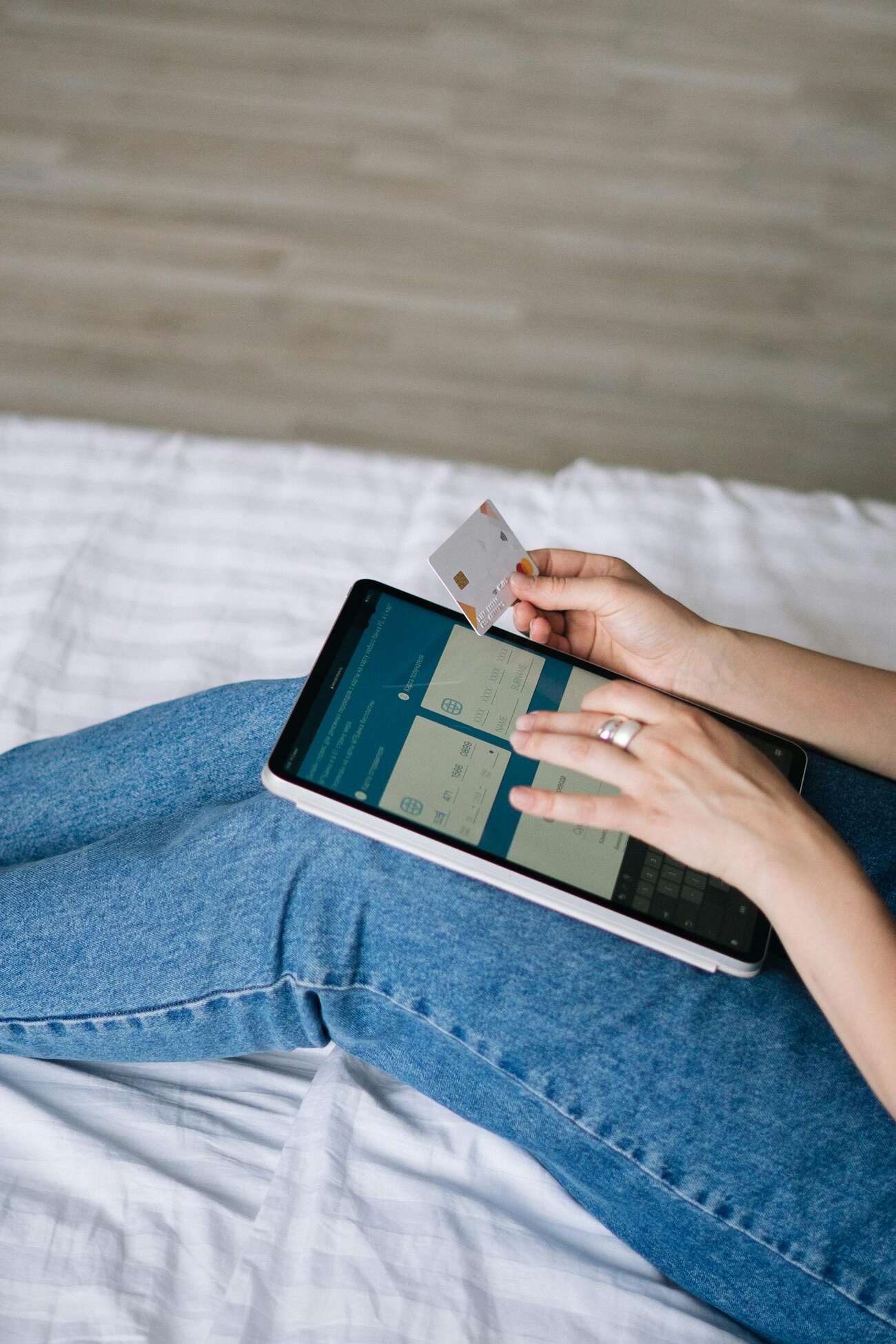 A woman sitting on a bed, holding a credit card, ready for online shopping or making a payment