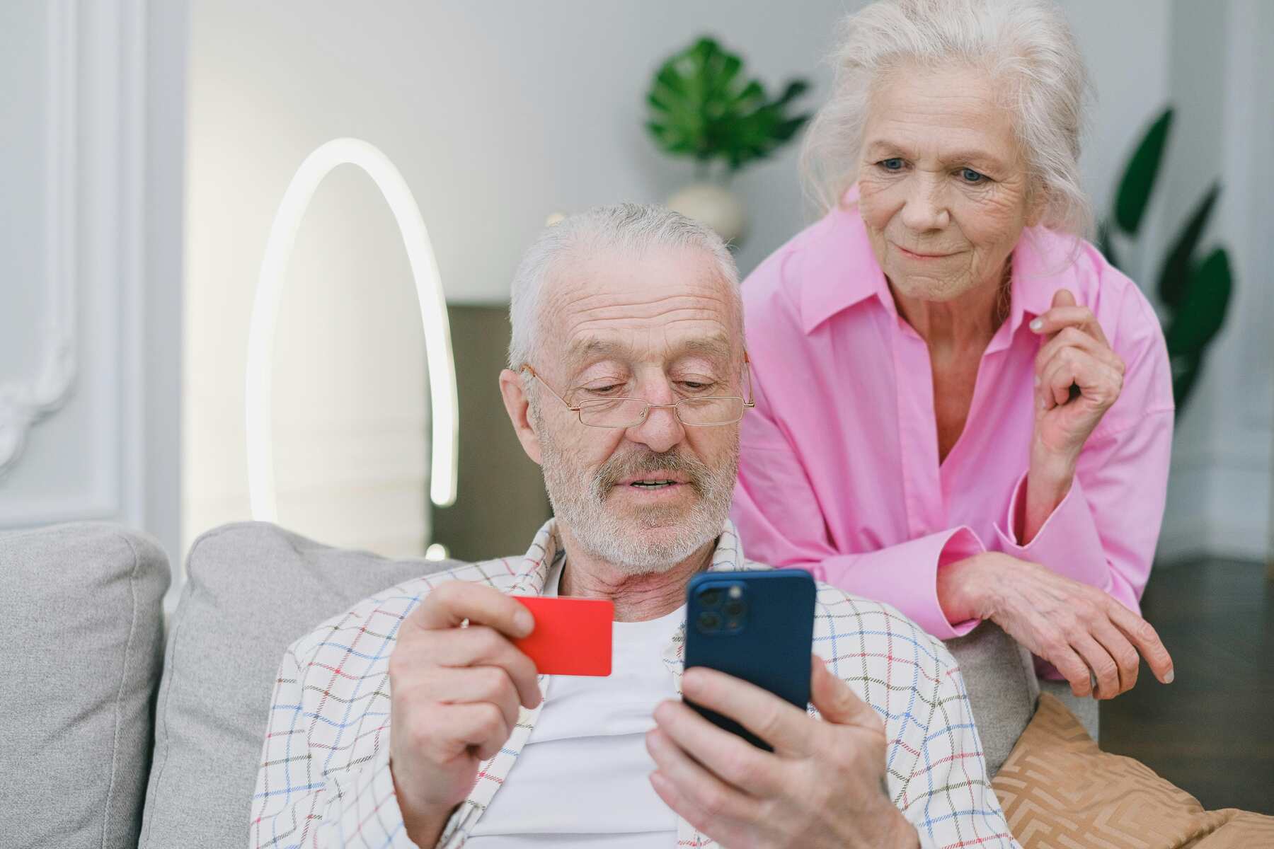 Two elderly looking at the phone while the husband is holding the credit card