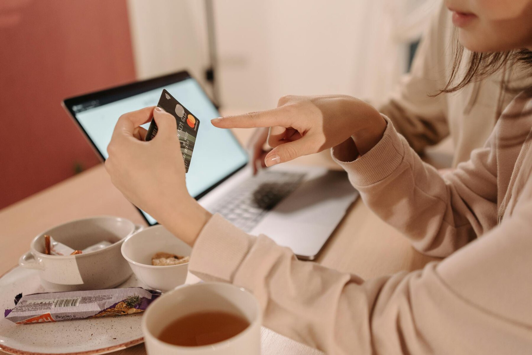 Woman pointing to a credit card she is holding with a laptop and food on the desk
