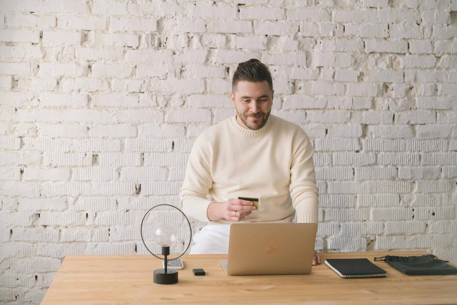 A man happily browsing on his laptop while holding his credit card