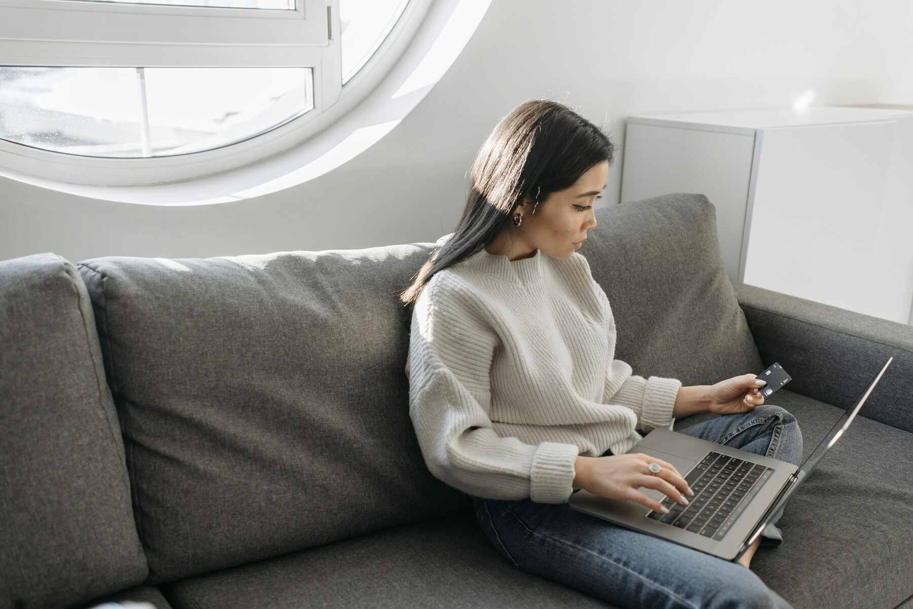 A woman sitting on a couch using her laptop and holding her credit card