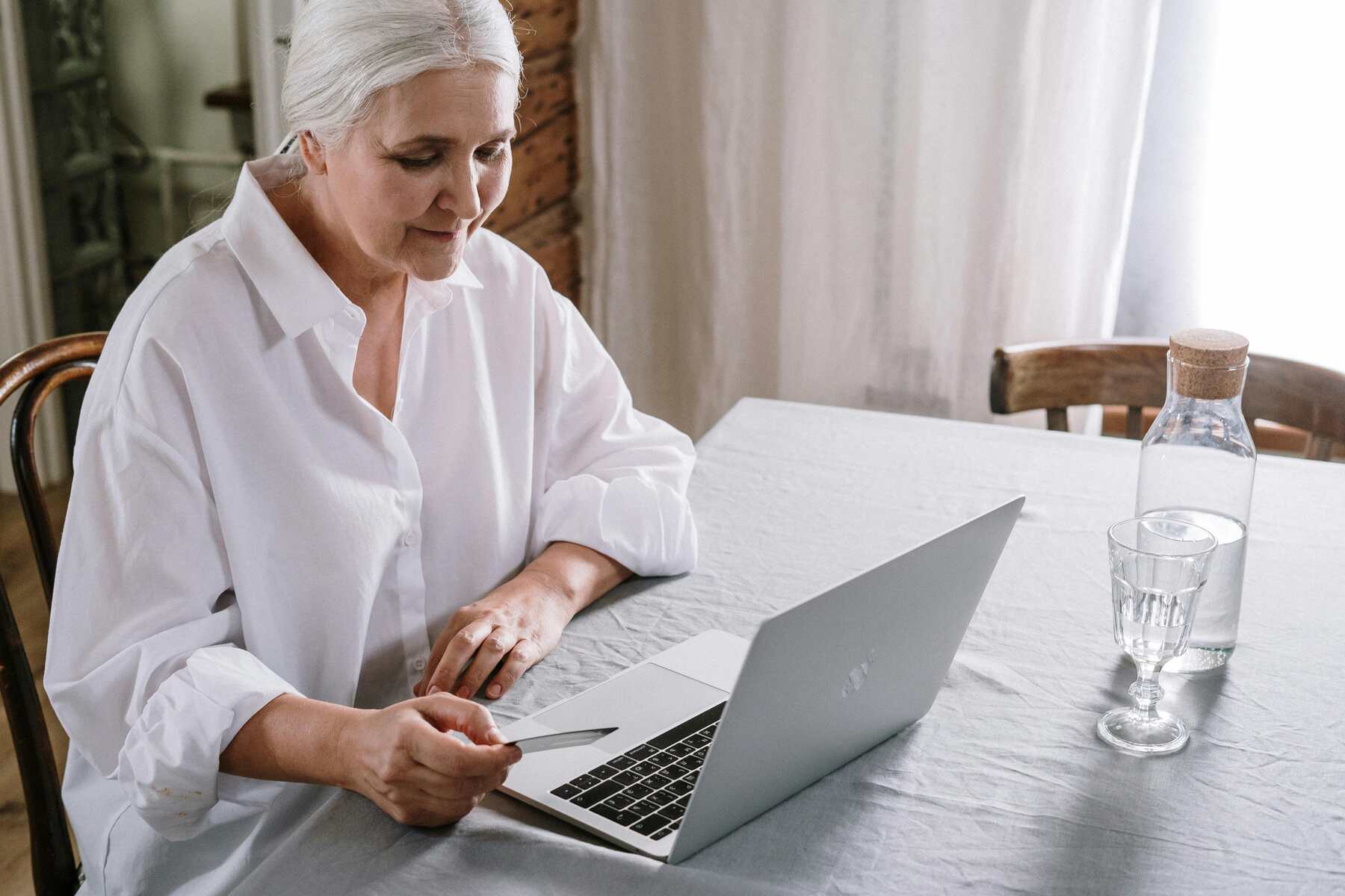 An elderly holding her credit card while looking at the laptop