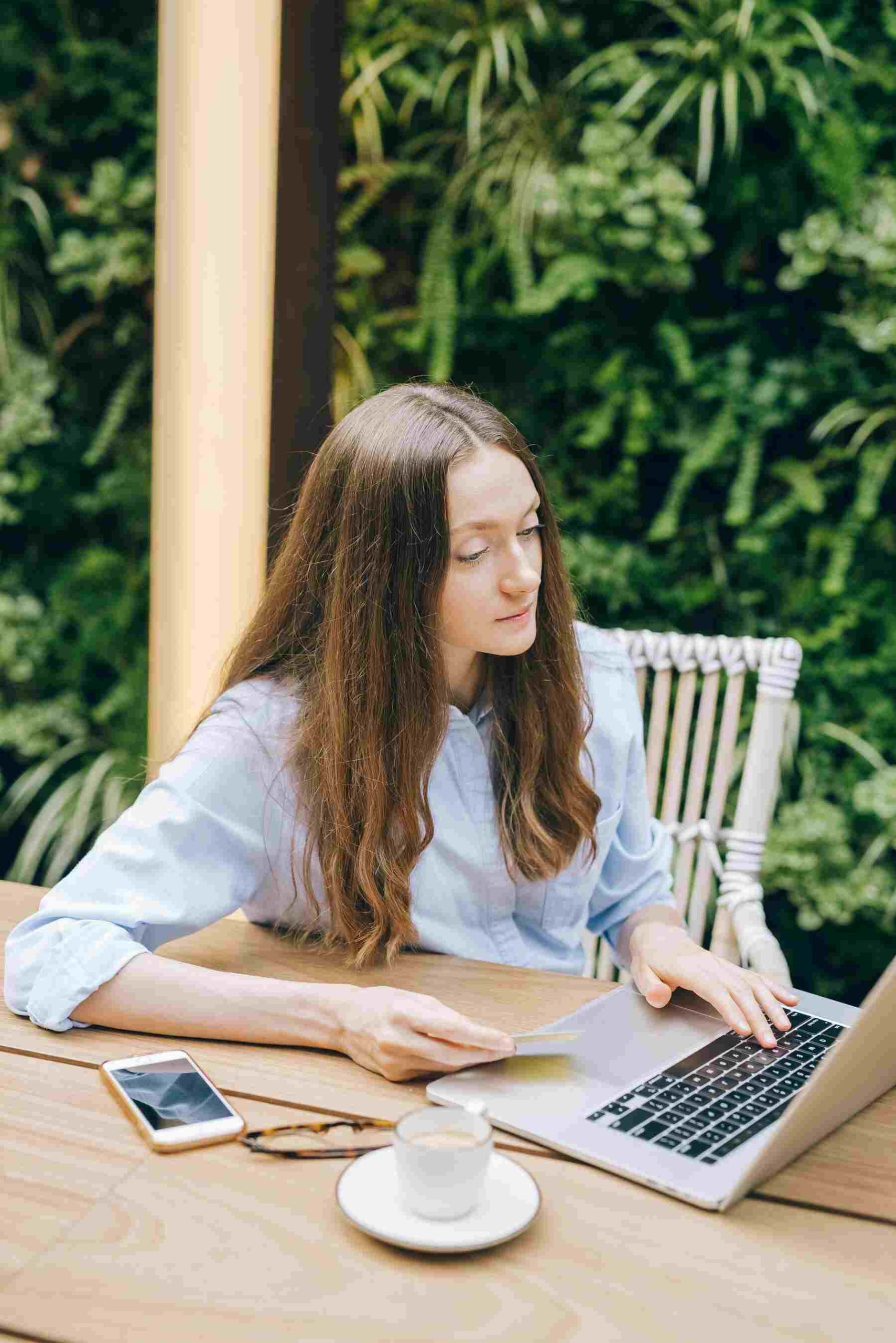 A woman sitting on the table outside typing on her laptop and holding her credit card