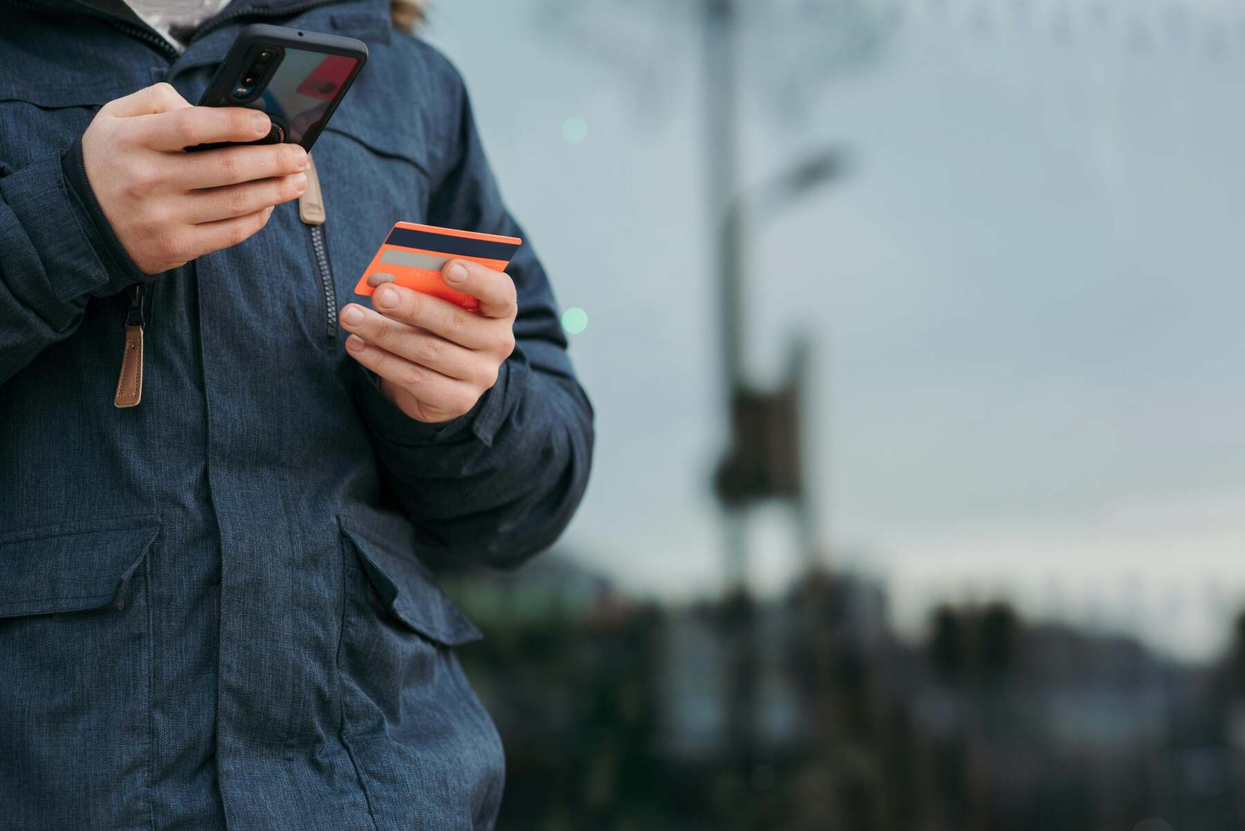 A man outside holding an orange credit card and phone