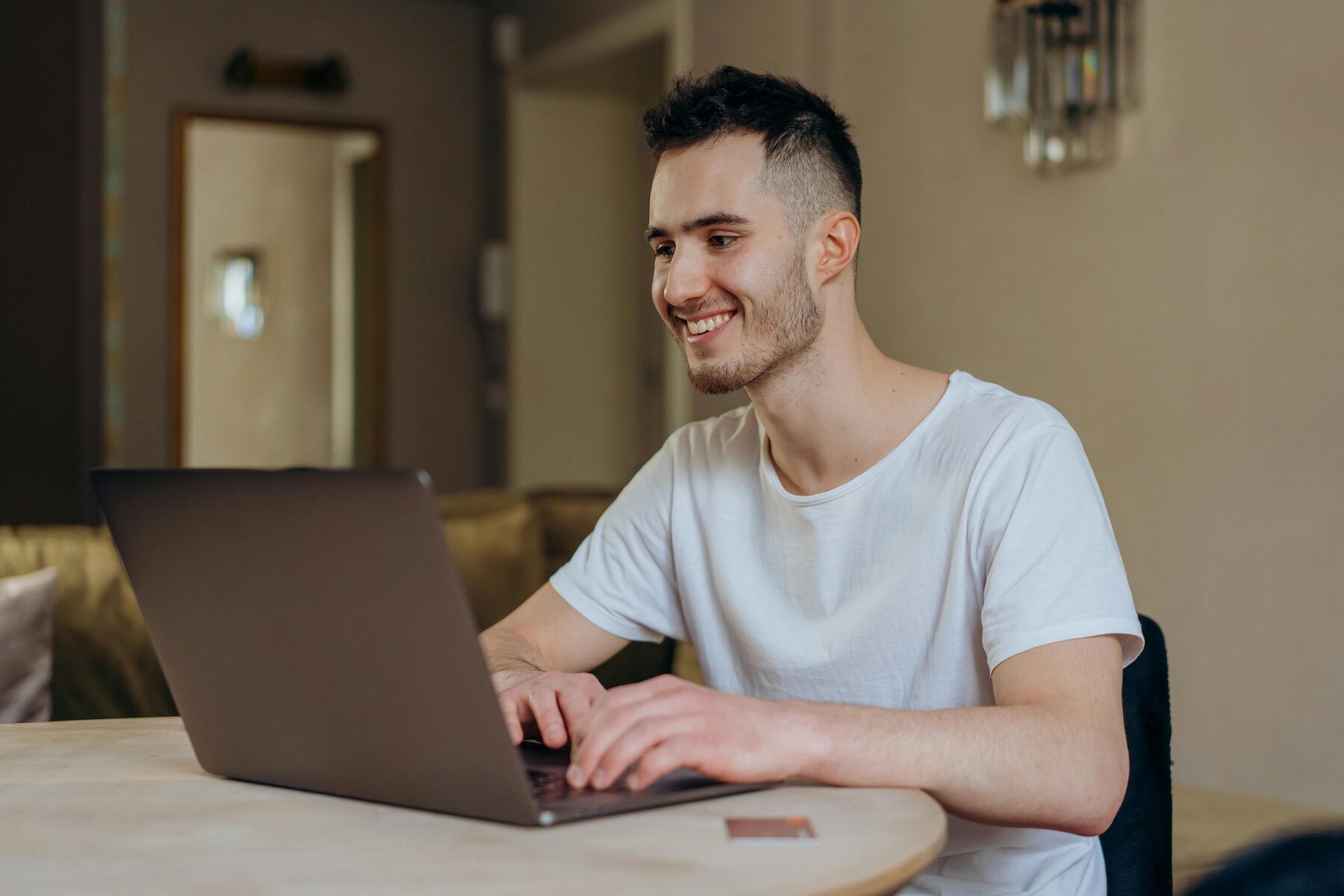 A man smiling while looking at his laptop with a credit card on the table